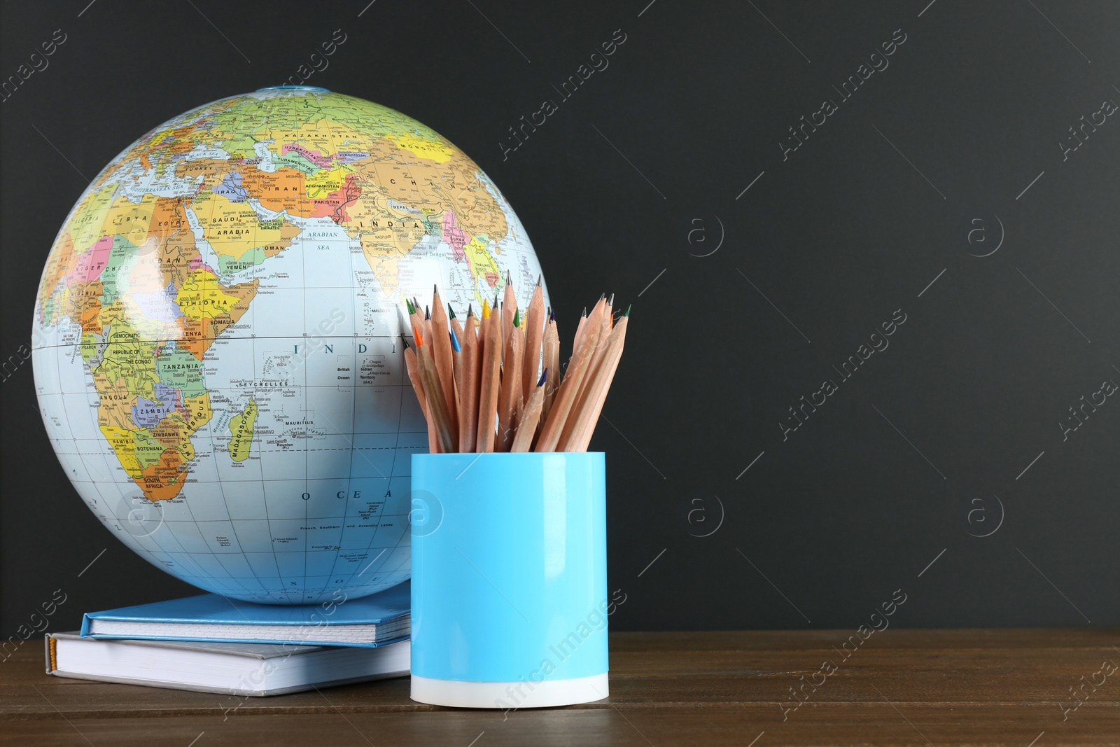 Photo of Globe, books and school supplies on wooden table near black chalkboard, space for text. Geography lesson