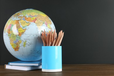 Photo of Globe, books and school supplies on wooden table near black chalkboard, space for text. Geography lesson