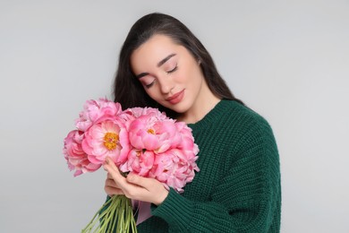 Photo of Beautiful young woman with bouquet of peonies on light grey background