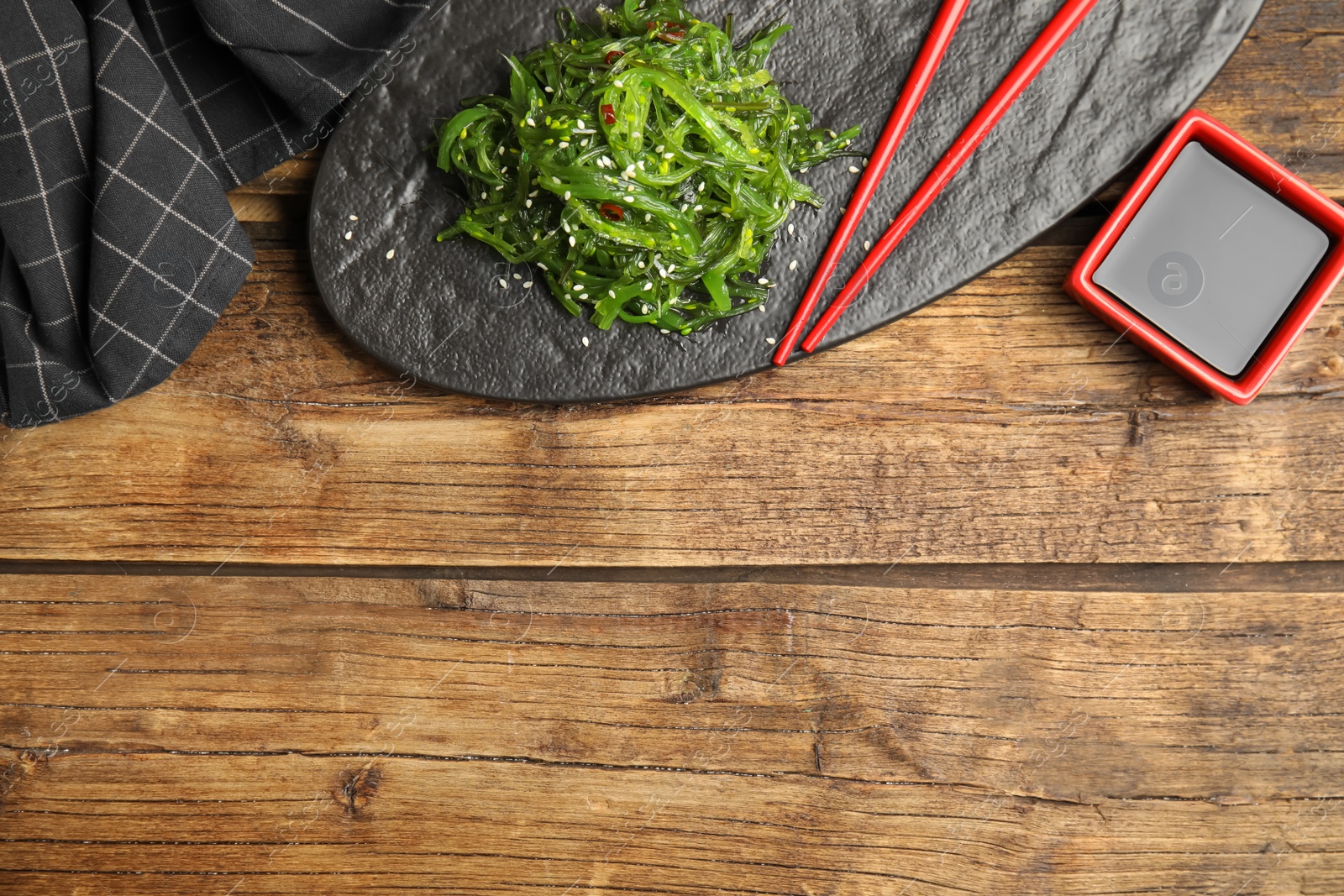 Photo of Japanese seaweed salad served on wooden table, flat lay. Space for text