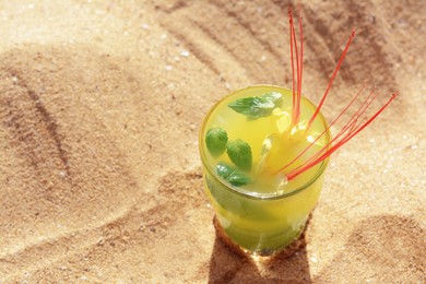 Photo of Glass of refreshing drink on sand. Space for text