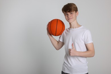 Photo of Teenage boy with basketball ball showing thumbs up on light grey background. Space for text