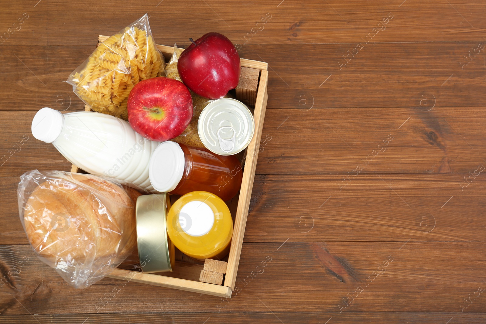 Photo of Humanitarian aid. Different food products for donation in crate on wooden table, top view. Space for text