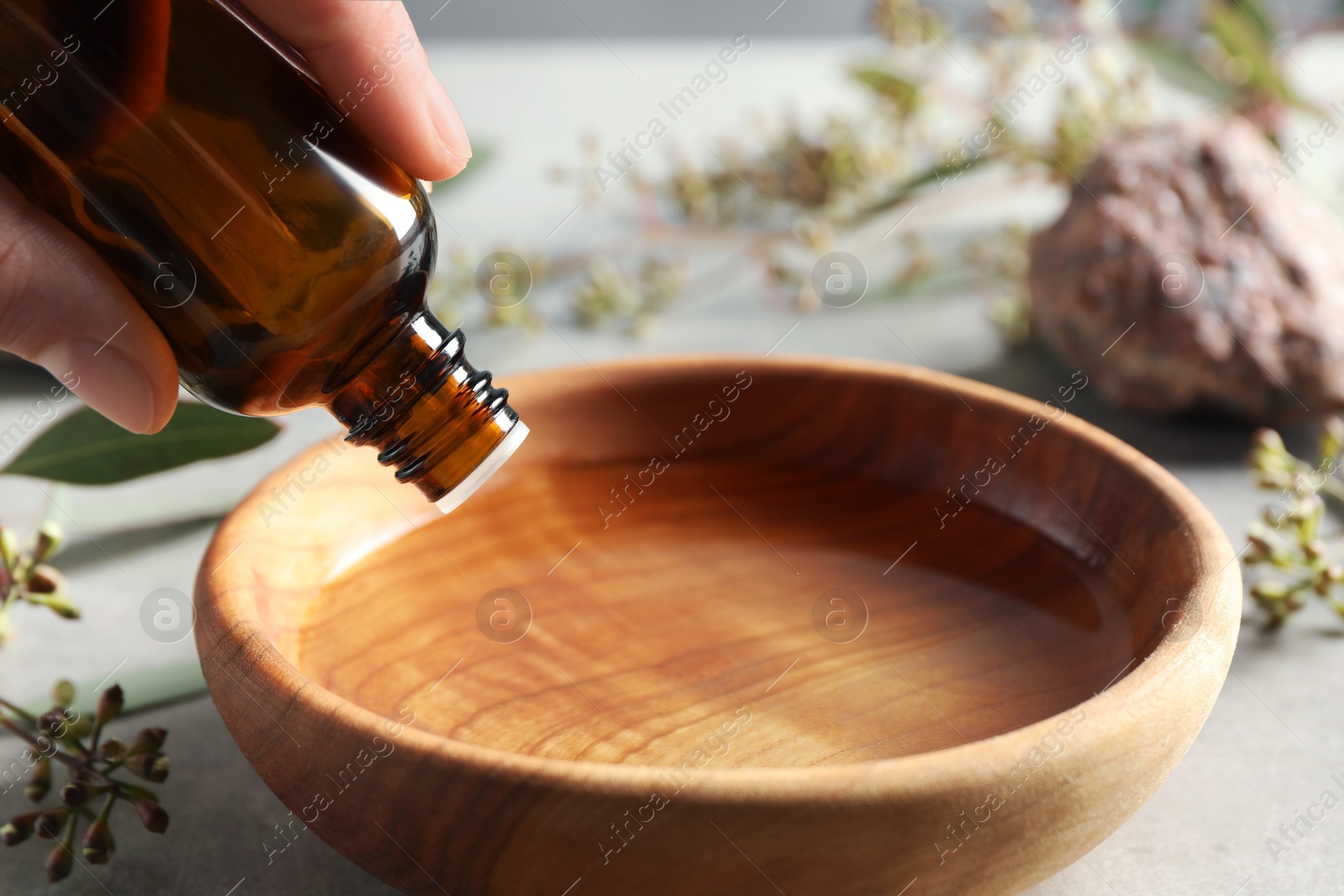 Photo of Woman dripping eucalyptus essential oil from bottle into bowl at light grey table, closeup