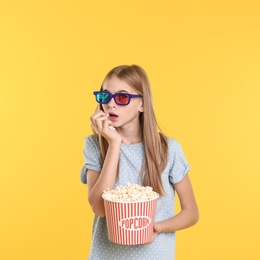 Emotional teenage girl with 3D glasses and popcorn during cinema show on color background