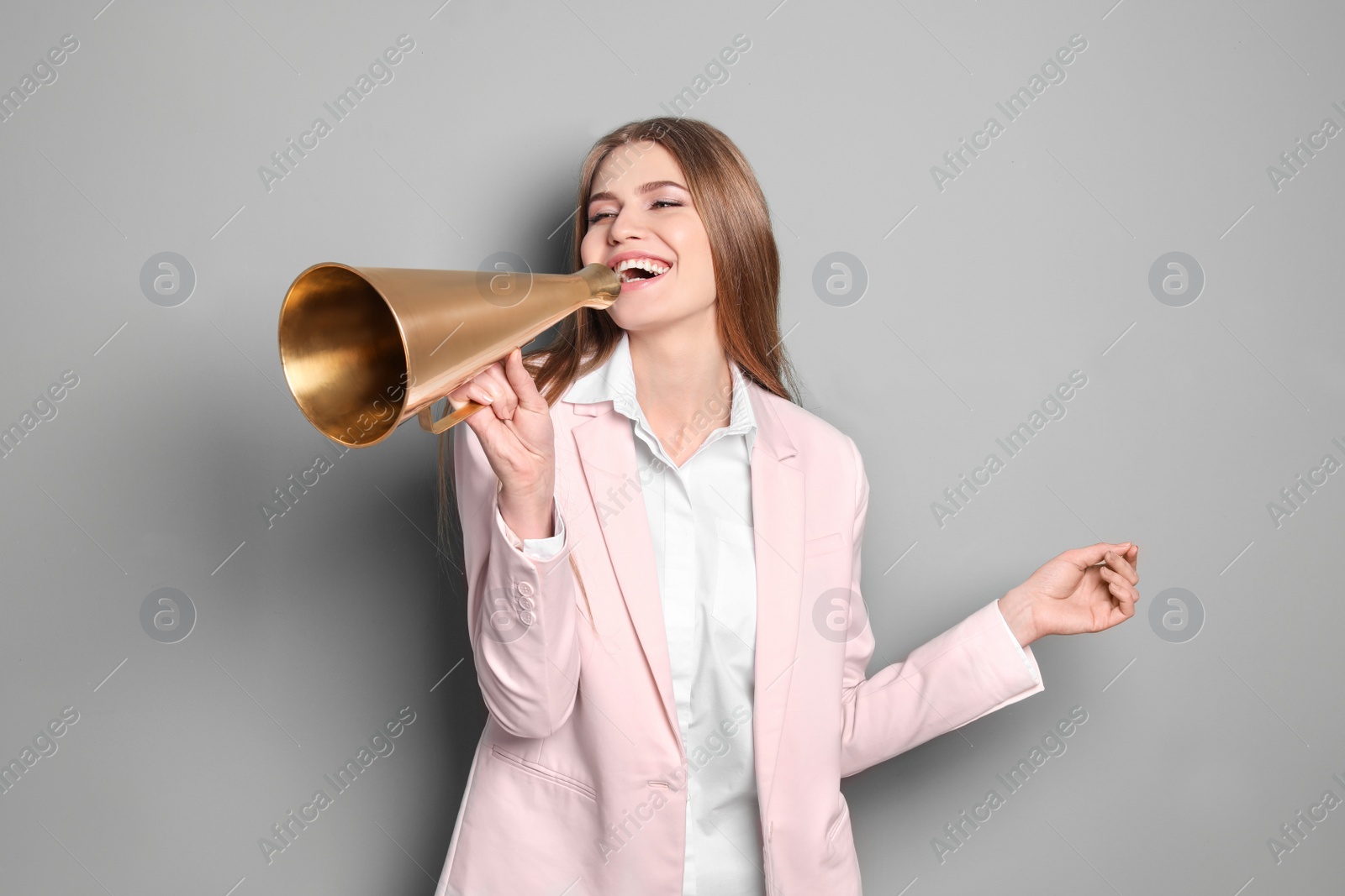 Photo of Young woman using megaphone on grey background