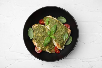 Delicious chicken breasts with pesto sauce, tomatoes and basil on white textured table, top view