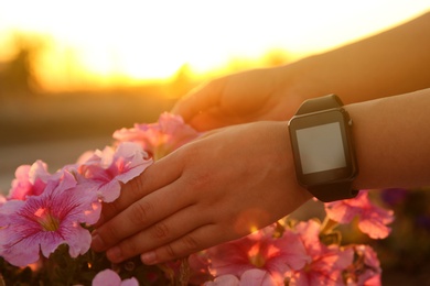 Woman with smartwatch near pink flowers outdoors in evening, closeup
