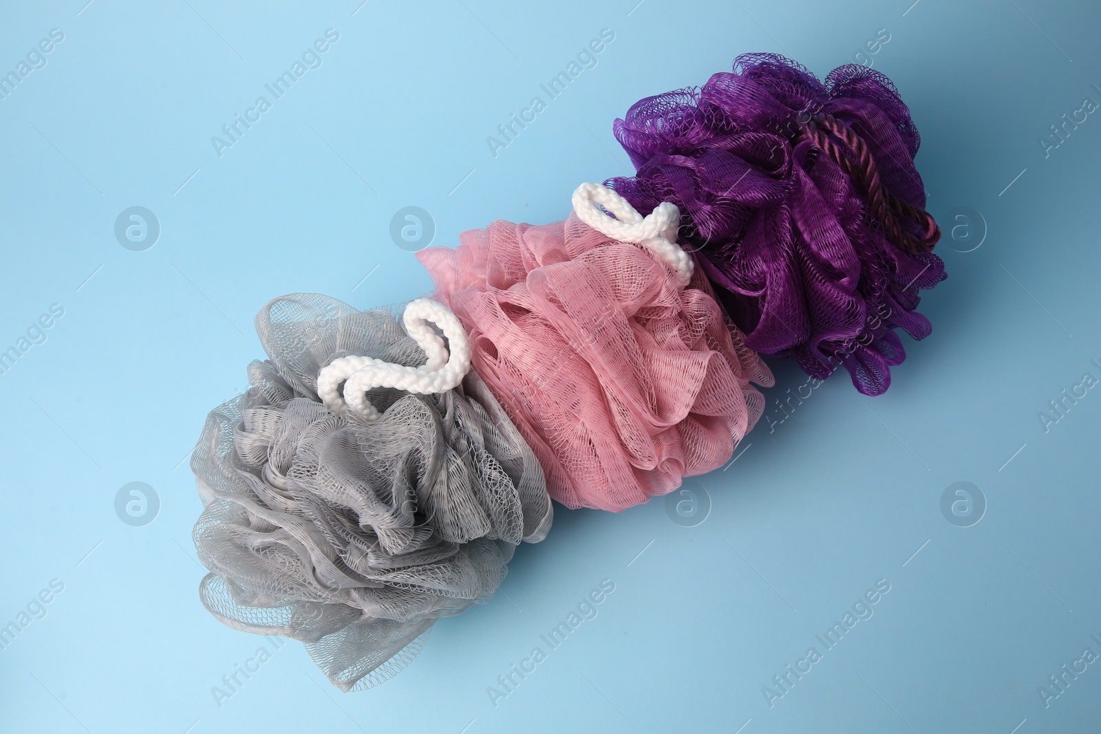 Photo of Colorful shower puffs on light blue background, flat lay