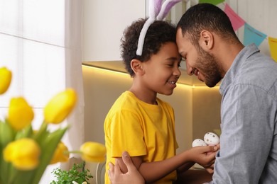 Photo of Happy African American father and his cute son with Easter eggs touching foreheads in kitchen