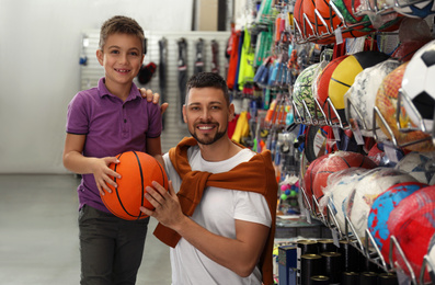 Photo of Little school boy with father choosing ball in supermarket