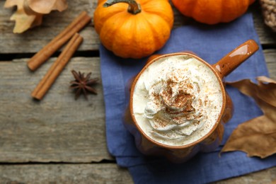 Photo of Mug of pumpkin spice latte with whipped cream, ingredients and dry leaves on wooden table, flat lay. Space for text