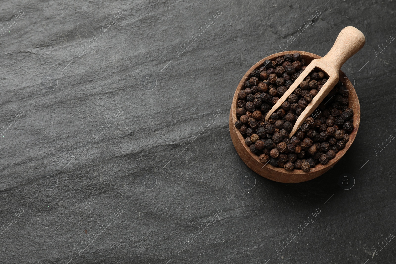 Photo of Aromatic spice. Pepper in bowl and scoop on black table, top view. Space for text