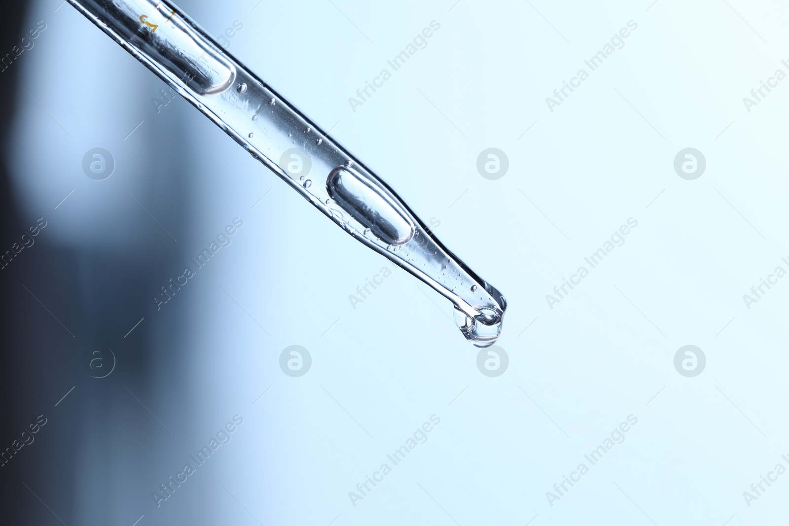 Photo of Dripping liquid from pipette on light blue background, closeup