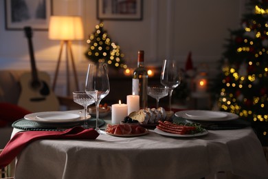 Photo of Christmas table setting with burning candles, appetizers and dishware in room