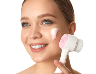 Photo of Young woman washing face with brush and cleansing foam on white background. Cosmetic products
