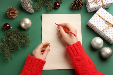 Photo of Top view of woman writing letter to Santa at green table, closeup