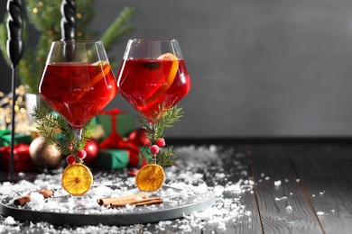 Photo of Christmas Sangria cocktail in glasses and snow on dark wooden table, space for text