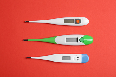 Photo of Modern digital thermometers on red background, flat lay