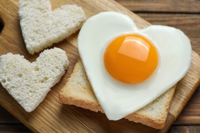 Heart shaped fried egg with toasts on wooden table, closeup