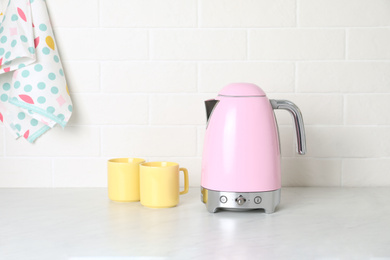 Modern electric kettle and cups on counter in kitchen