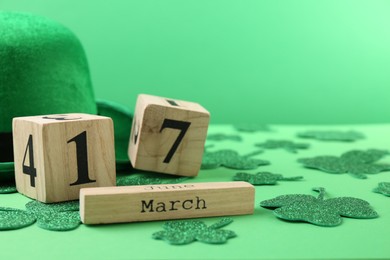 Photo of St. Patrick's day - 17th of March. Wooden block calendar, leprechaun hat and decorative clover leaves on green background. Space for text