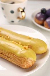 Tasty glazed eclairs on white table, closeup