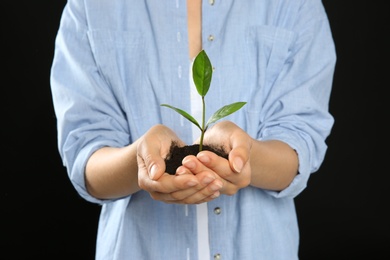 Photo of Woman holding soil with green plant in hands on black background