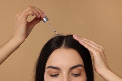 Photo of Woman applying hair serum on beige background, closeup. Cosmetic product