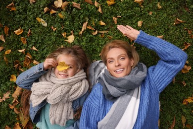 Photo of Portrait of happy mother and her daughter on green grass with autumn leaves outdoors, top view