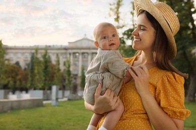 Happy mother with adorable baby walking in park on sunny day, space for text