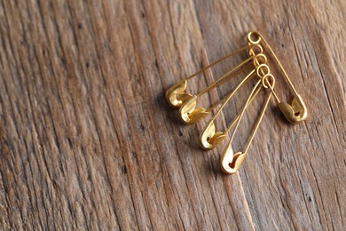 Golden safety pins on wooden table, flat lay. Space for text