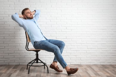 Photo of Young man relaxing in office chair near white brick wall indoors, space for text