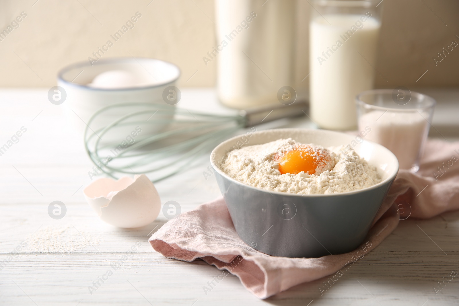 Photo of Making dough. Flour with yolk in bowl on white wooden table, closeup