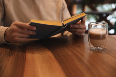 Man with coffee reading book at wooden table, closeup