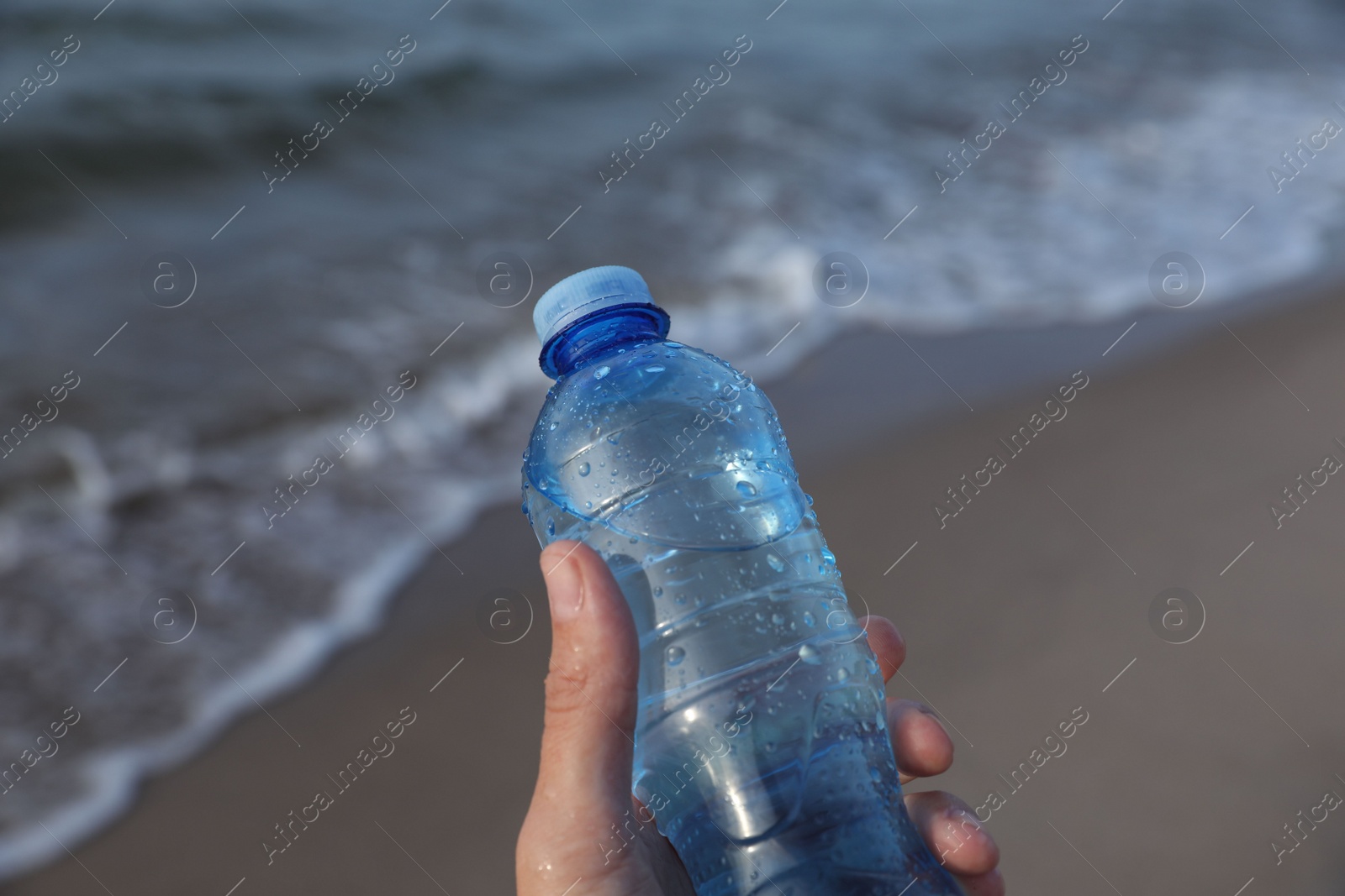 Photo of Woman holding plastic bottle with water near sea, closeup