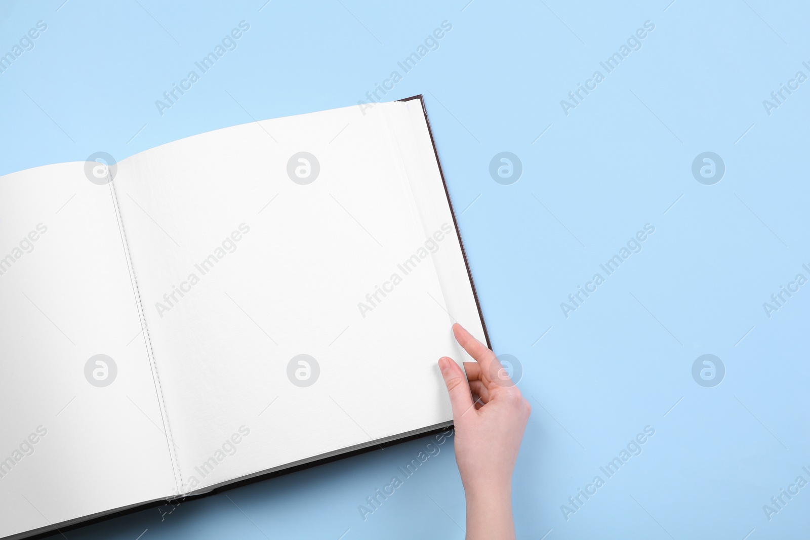 Photo of Woman with open photo album at light blue background, top view. Space for text