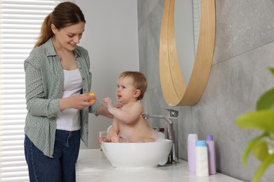 Mother washing her little baby in sink at home