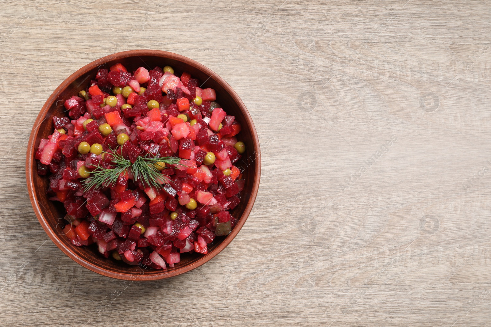 Photo of Bowl of delicious fresh vinaigrette salad on wooden table, top view. Space for text