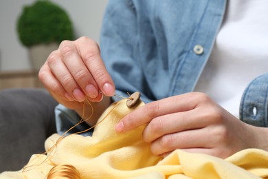 Woman sewing button with needle and thread onto shirt at home, closeup