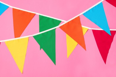 Photo of Buntings with colorful triangular flags on pink background. Festive decor