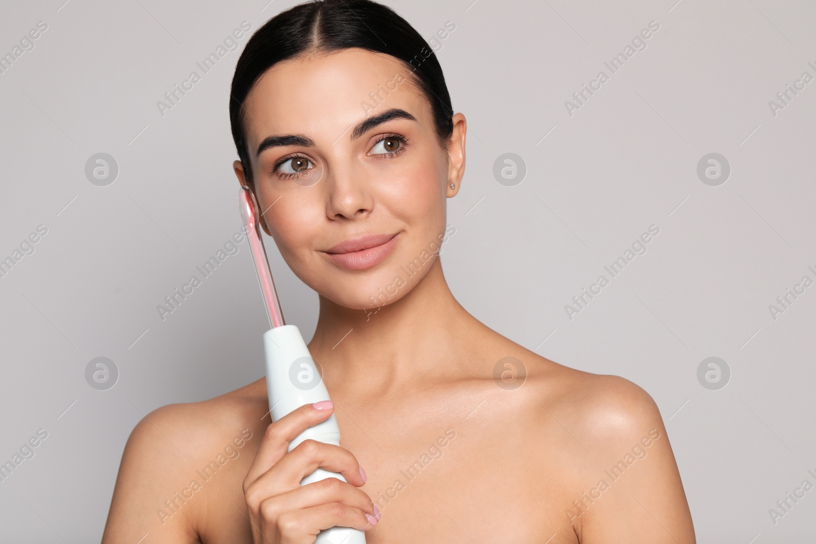 Photo of Woman using high frequency darsonval device on grey background