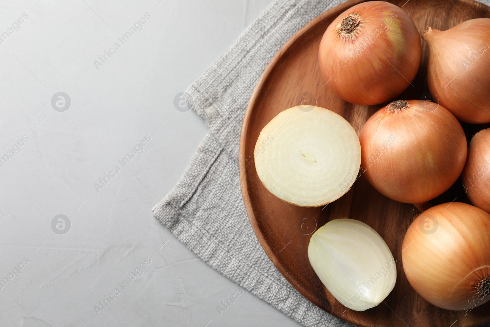 Photo of Whole and cut onions on light grey textured table, top view. Space for text