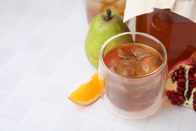 Photo of Tasty kombucha with ice cubes and fresh fruits on white tiled table, space for text