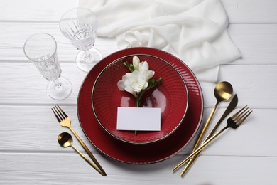 Stylish table setting. Dishes, cutlery, blank card and floral decor on white wooden background, flat lay