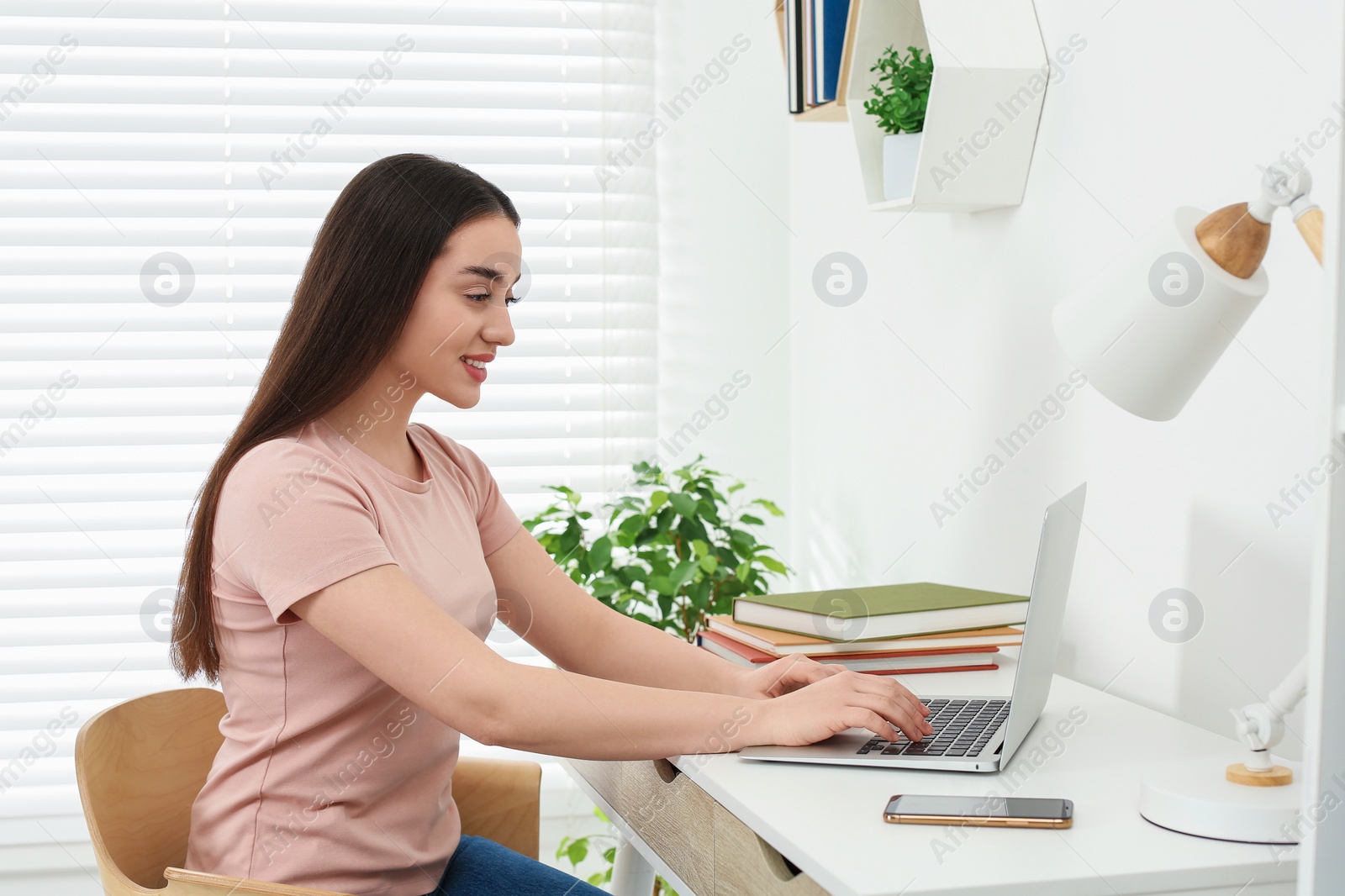 Photo of Home workplace. Woman working on laptop at white desk in room