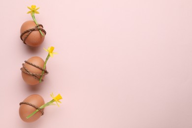 Photo of Easter eggs decorated with flowers on pale pink background, top view. Space for text