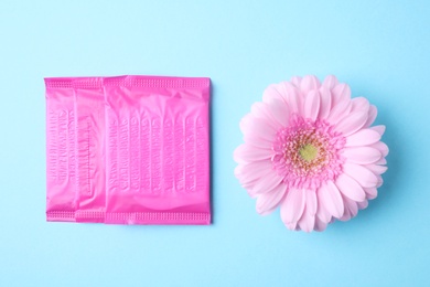 Photo of Packed menstrual pads and flower on color background, flat lay. Gynecological care