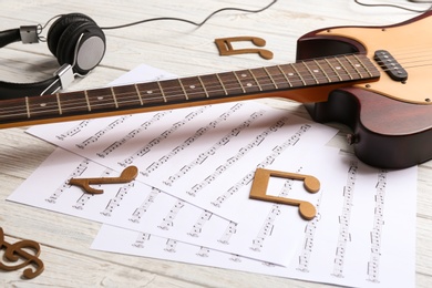 Music notes, headphones and guitar on white wooden table