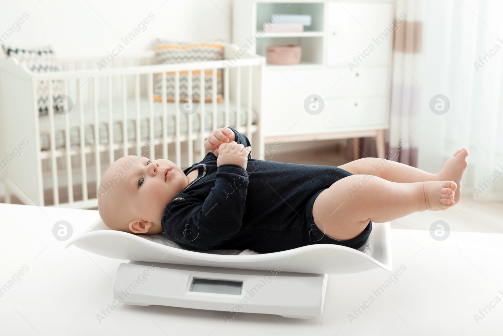 Photo of Cute little baby lying on scales in light room